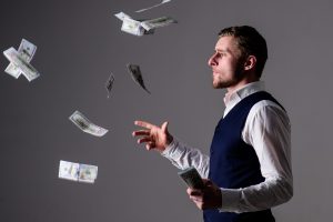 Richness and wealth concept. Successful entrepreneur on arrogant face wasting money. Man in formal wear, businessman throwing money on grey background. Banknotes, cash dollars fly in air around guy.