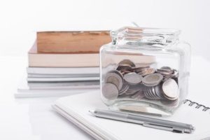 Book, pen with penny jar filled with coins money on white background. education financing concept