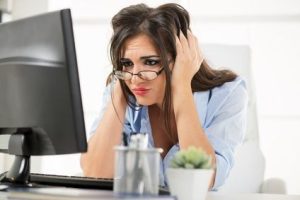 Businesswoman with a sad expression on her face sitting in front computer leaning on office desk with her hands on her head.