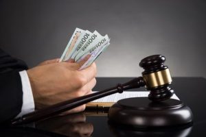 Close-up Of Judge Hands Counting Banknote In Front Of Gavel At Desk