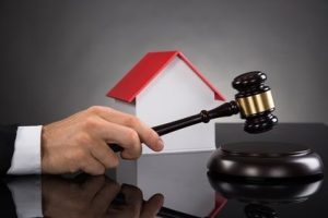 Close-up Of Judge With House Model Hitting Gavel At Desk