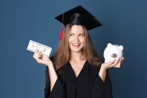 Young graduate with piggy bank on color background