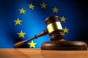 European Union law, legislation and parliament concept with a 3d rendering of a gavel on a wooden desktop and the EU flag on background.