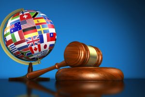 International law systems, justice, human rights and global business education concept with world flags on a school globe and a gavel on a desk on blue background.